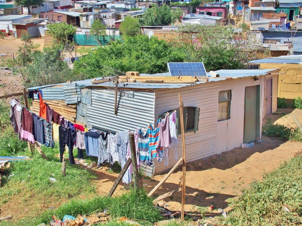 A shack in an informal settlement with a solar panel on the roof.